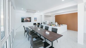 A modern dining area with a long table, chairs, and a kitchen counter. - Eng Fah Luang Hotel (Chiang Rai)
