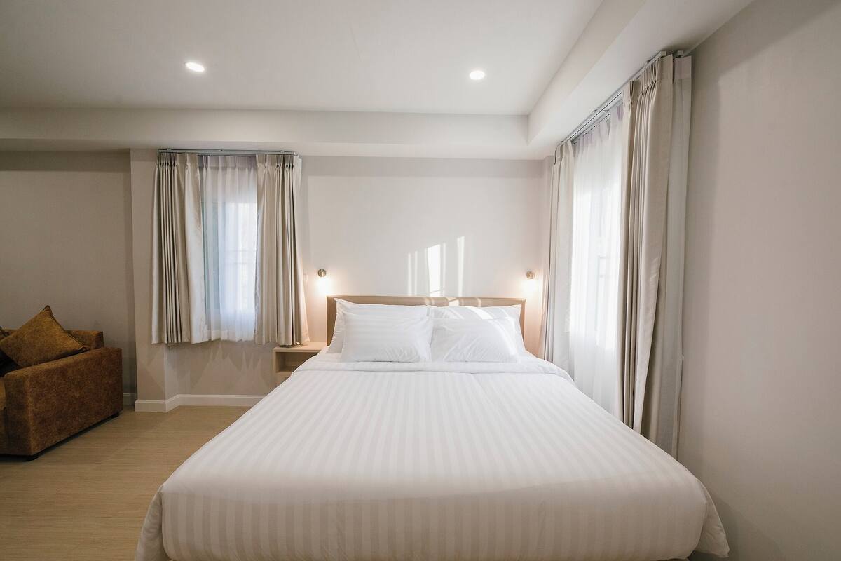 A hotel room with a large bed, two bedside tables, a nightstand, and a brown armchair.