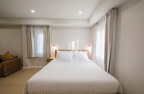 A hotel room with a large bed, two bedside tables, a nightstand, and a brown armchair. - Eng Fah Luang Hotel (Chiang Rai)