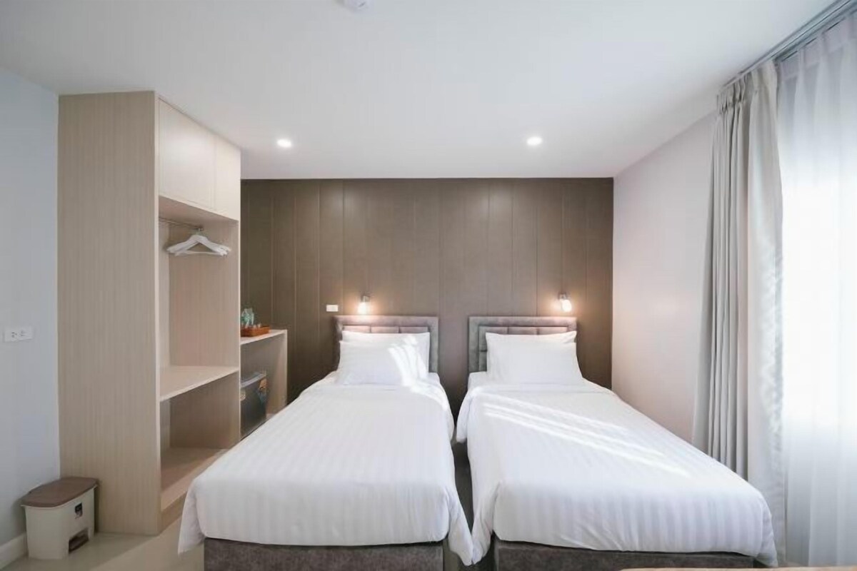 A hotel room with two single beds, a wardrobe, and a small table.