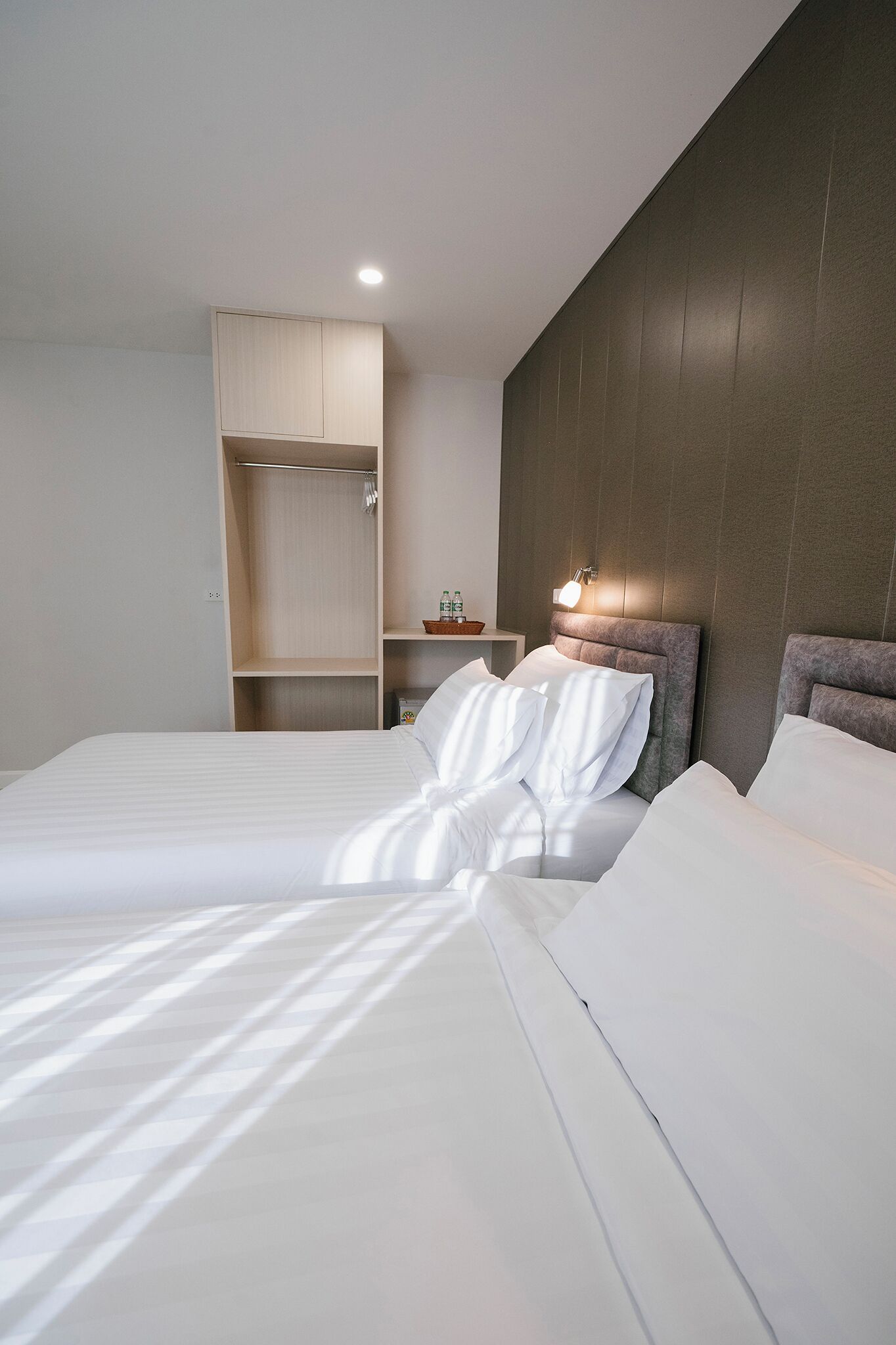 A neatly made bed with white linens, a wooden wardrobe, and a wall-mounted light fixture.