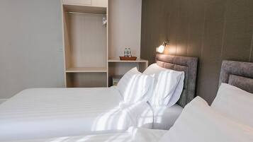 A neatly made bed with white linens, a wooden wardrobe, and a wall-mounted light fixture.