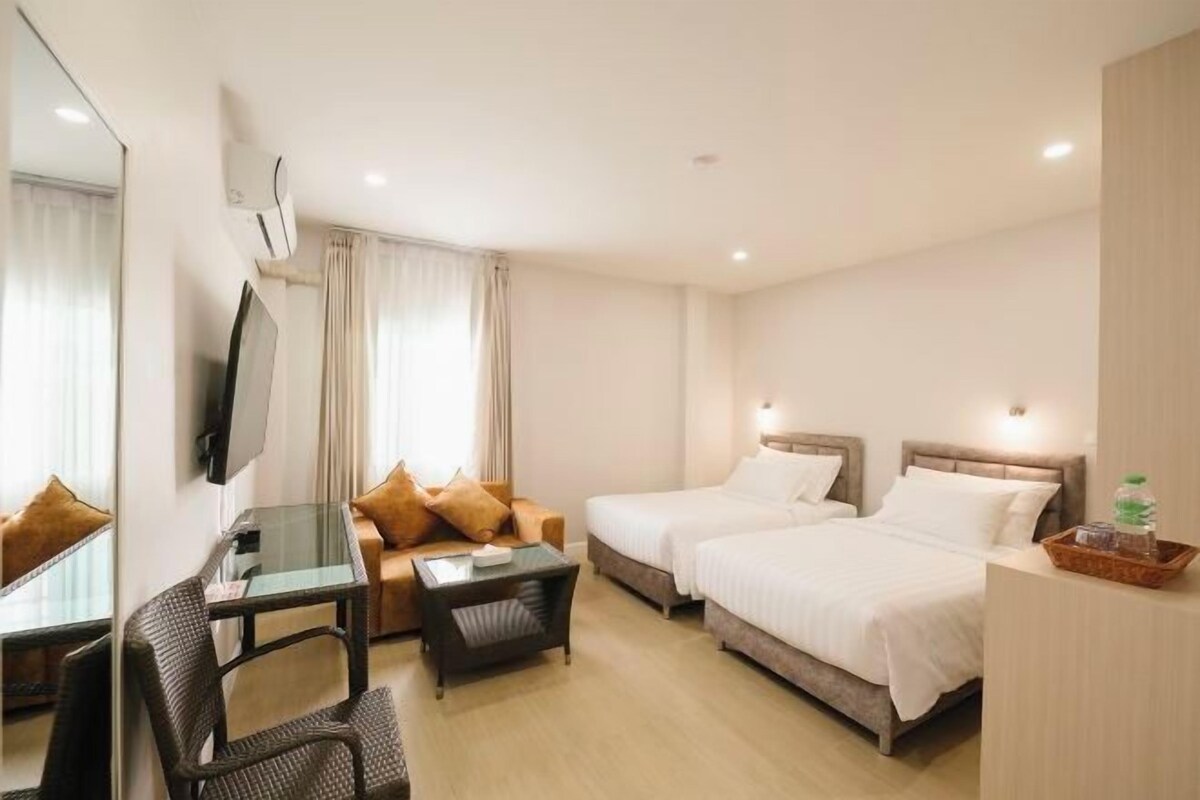 A hotel room with two beds, a desk with a chair, a TV, and a large mirror.