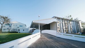 A modern building with a curved entrance, a covered walkway, and a white fence. - Eng Fah Luang Hotel (Chiang Rai)