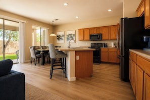 A modern kitchen with wooden cabinets, a black refrigerator, a microwave, and a dining area with chairs and a table.