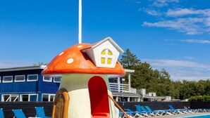 A colorful mushroom-shaped playhouse with a yellow window, located near a swimming pool with lounge chairs. - 6 Person Holiday Park Home in Vipperod (Vipperod)