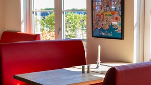 A dining area with red upholstered booths, a wooden table, and a framed artwork depicting a colorful scene with the word "Holbæk". - 6 Person Holiday Park Home in Vipperod (Vipperod)