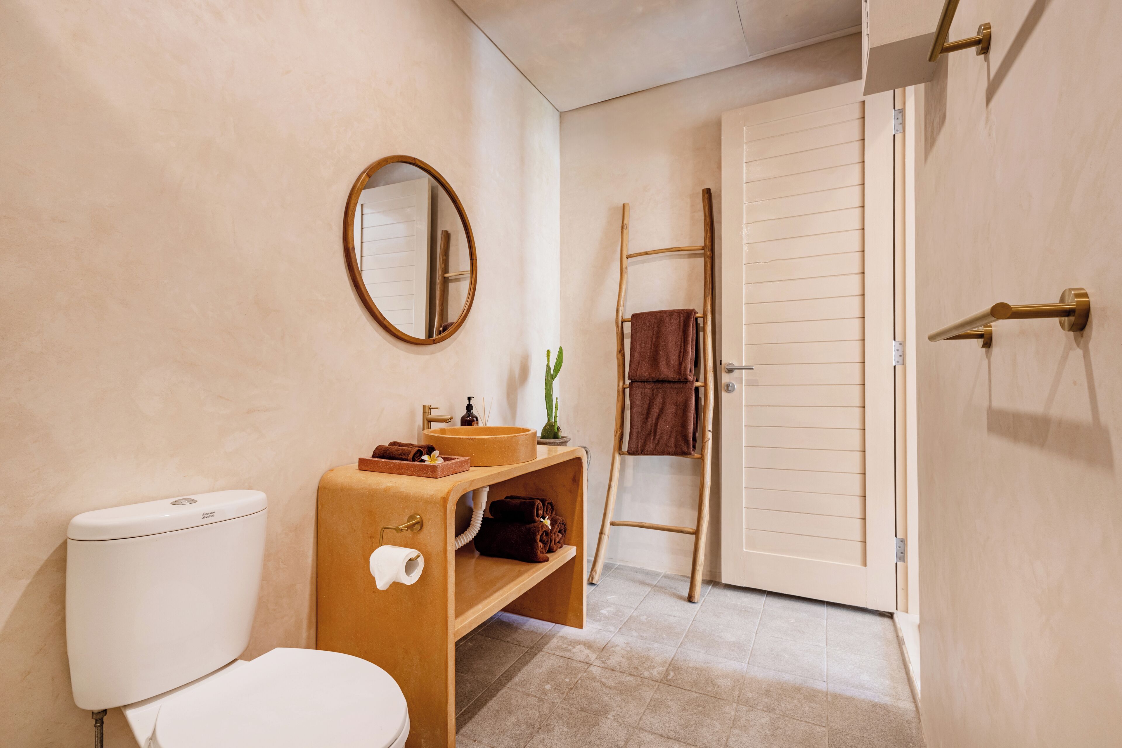 Une salle de bain équipée d’un WC, d’un lavabo, d’un miroir, d’un porte-serviettes et d’une étagère en bois.