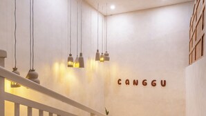 Un intérieur moderne avec un escalier, des suspensions lumineuses et un mur sur lequel est inscrit le nom « CANGGU ».