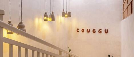 Un intérieur moderne avec un escalier, des suspensions lumineuses et un mur sur lequel est inscrit le nom « CANGGU ».