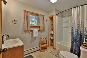 A bathroom with a sink, toilet, and shower. There is a window with curtains, a towel rack, and a wicker basket. - Lakeside Lodge at Fern Lake: 3BR/1BA Waterfront w/ Dock (Leicester)