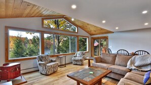 A spacious living room with large windows, a wooden ceiling, and a cozy seating area. - Lakeside Lodge at Fern Lake: 3BR/1BA Waterfront w/ Dock (Leicester)