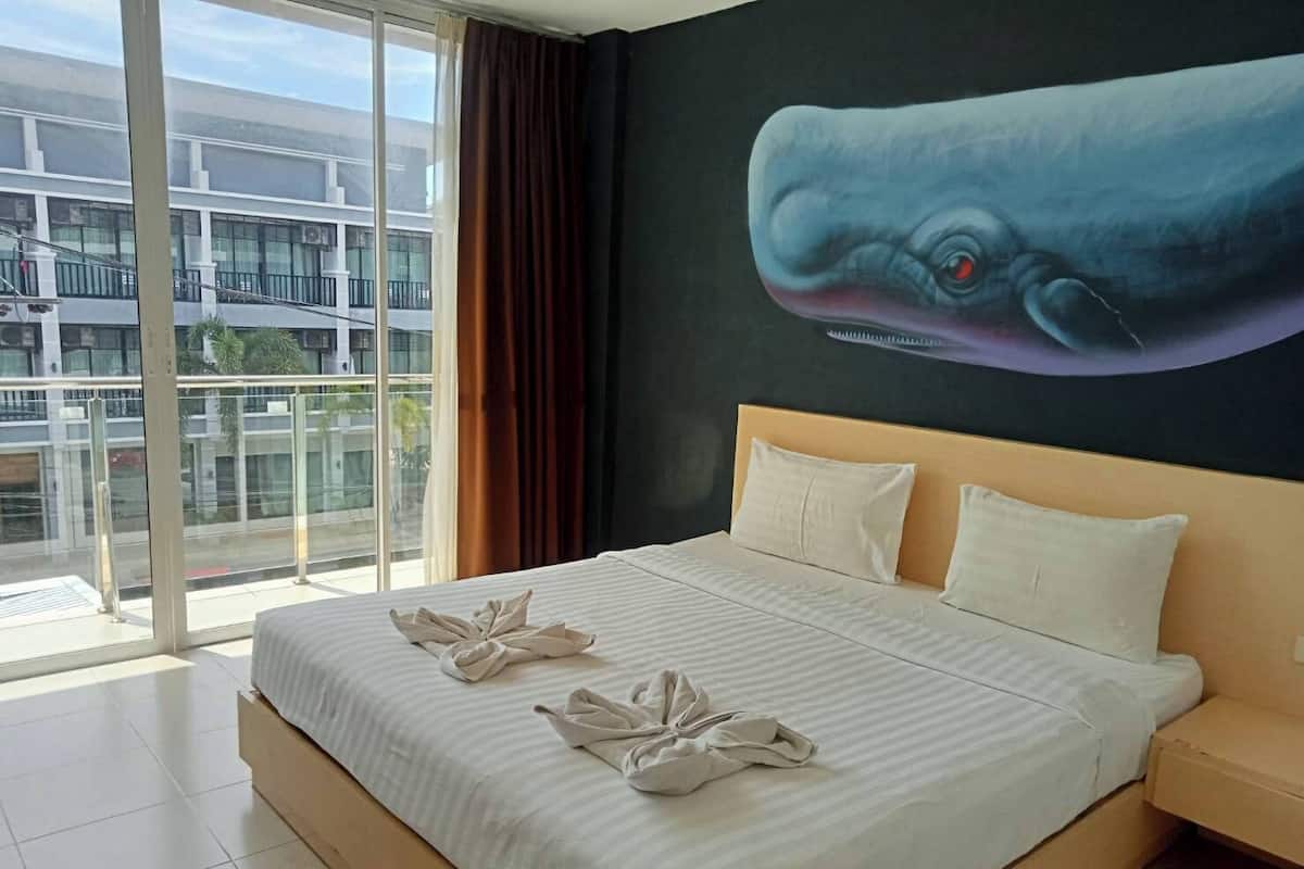 Hotelkamer met een groot bed, uitzicht op een gebouw door een glazen deur en een muurschildering van een waloog.