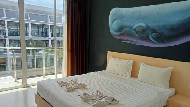 Un cuarto de hotel con una cama grande, vista de un edificio a través de una puerta de vidrio y un mural del ojo de una ballena en la pared.
