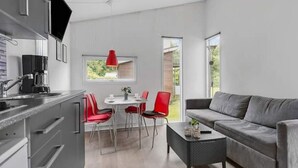 Une cuisine moderne avec un coin repas, un canapé gris et une suspension rouge.