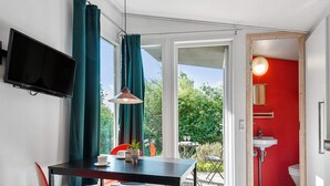 Une pièce de taille modeste comprenant une table à manger, des chaises, un téléviseur fixé au mur et une salle de bain aux murs rouges.