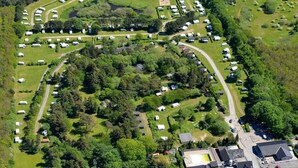 Una vista aerea di un campeggio con camper e case mobili disposti a semicerchio attorno a un'area verde centrale.