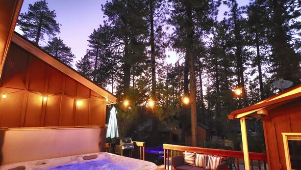 Un jacuzzi en una terraza de madera con vista a altos árboles al fondo.