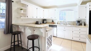Una cocina moderna con armarios blancos, encimeras de granito y dos taburetes de bar.