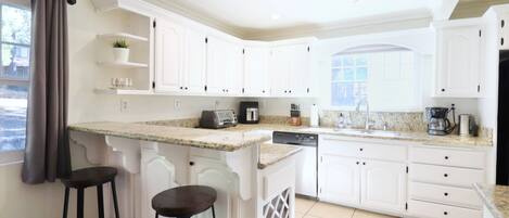Una cocina moderna con armarios blancos, encimeras de granito y dos taburetes de bar.