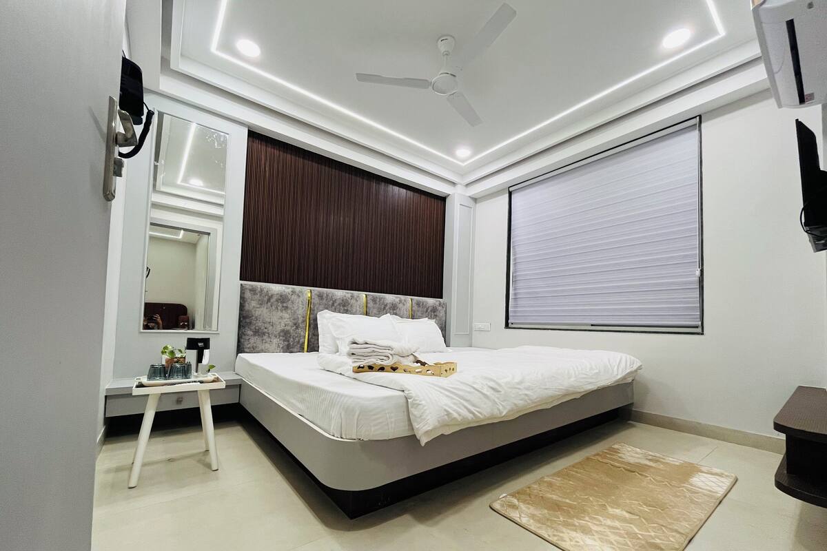 Une chambre moderne avec un lit, une table de chevet, un miroir et une grande fenêtre équipée de stores.