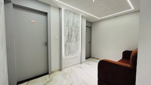 A modern hallway with marble flooring, a brown upholstered bench, and a door with a number plate. - Hotel Padmawati Palace (Ujjain)