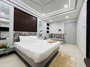 A modern bedroom with a large bed, bedside tables, a bench, a ceiling fan, and a door.