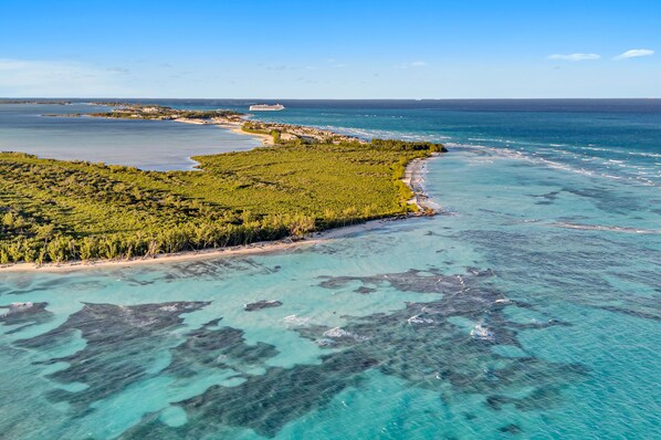 Vista aérea de una zona costera con aguas turquesas cristalinas, una playa de arena y vegetación verde exuberante.
