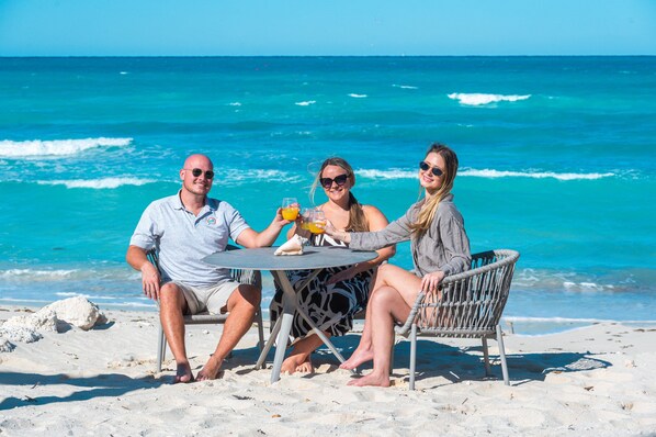 Three people seated at a round table on a beach with a view of the ocean.