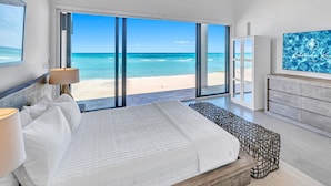 A bedroom with a large bed, a bench, a TV, and a view of the beach.