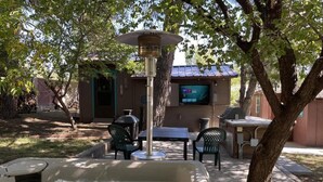 A hot tub surrounded by outdoor furniture, a barbecue grill, and a television screen. - Midtown Meadow Cabin (Ruidoso)