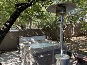 Un bain à remous équipé d’un système de chauffage solaire, entouré d’arbres et délimité par un mur en béton.