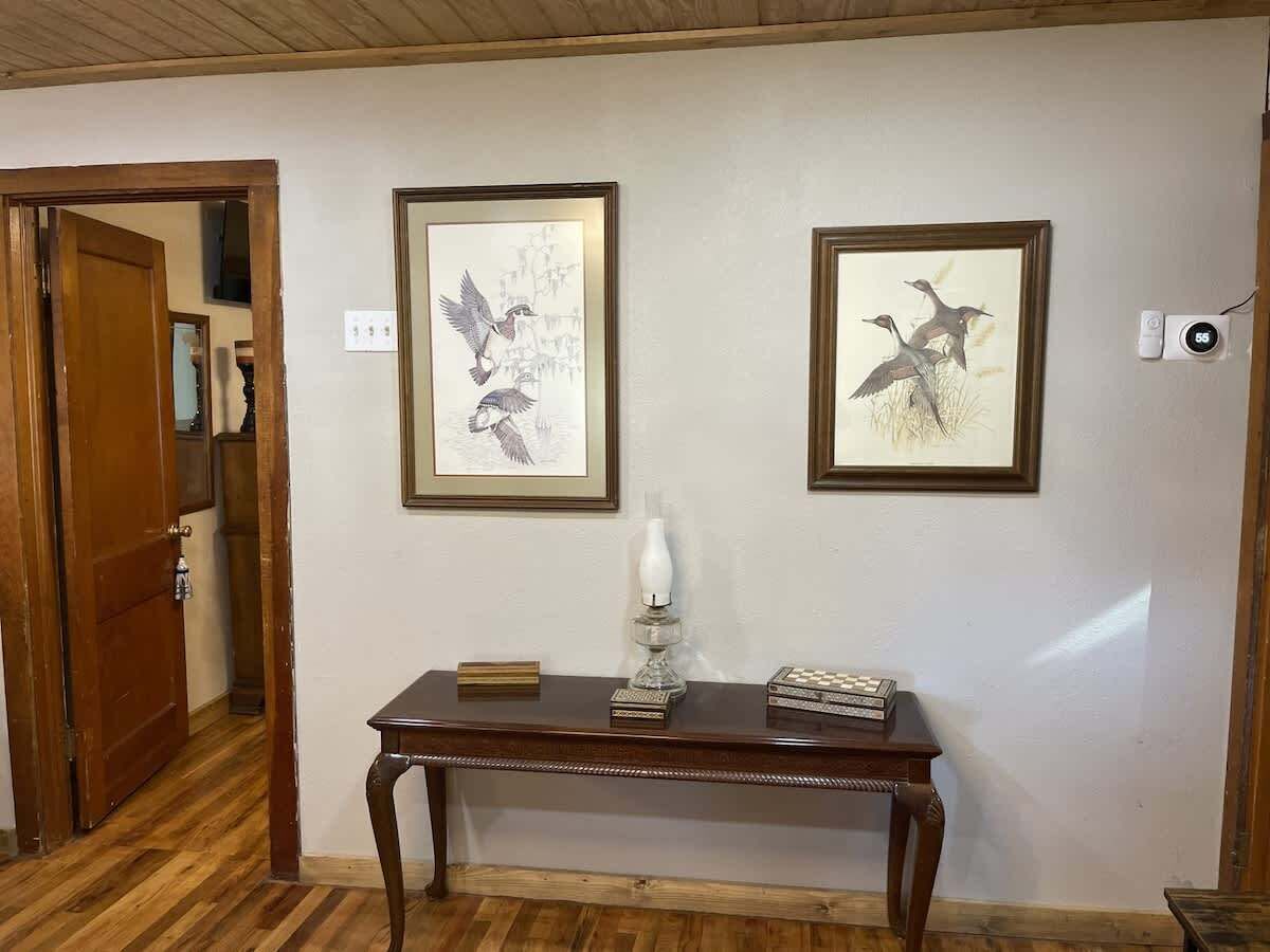 A hallway with wooden flooring, a wooden door, and two framed wall art pieces depicting birds.
