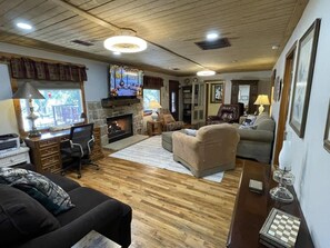 Un salon chaleureux avec une cheminée, un plancher en bois, un bureau et des sièges confortables.