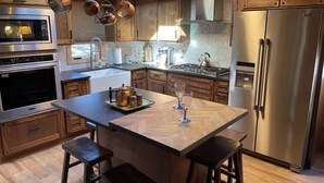 A modern kitchen with wooden cabinets, stainless steel appliances, and a central island with stools. - Midtown Meadow Cabin (Ruidoso)