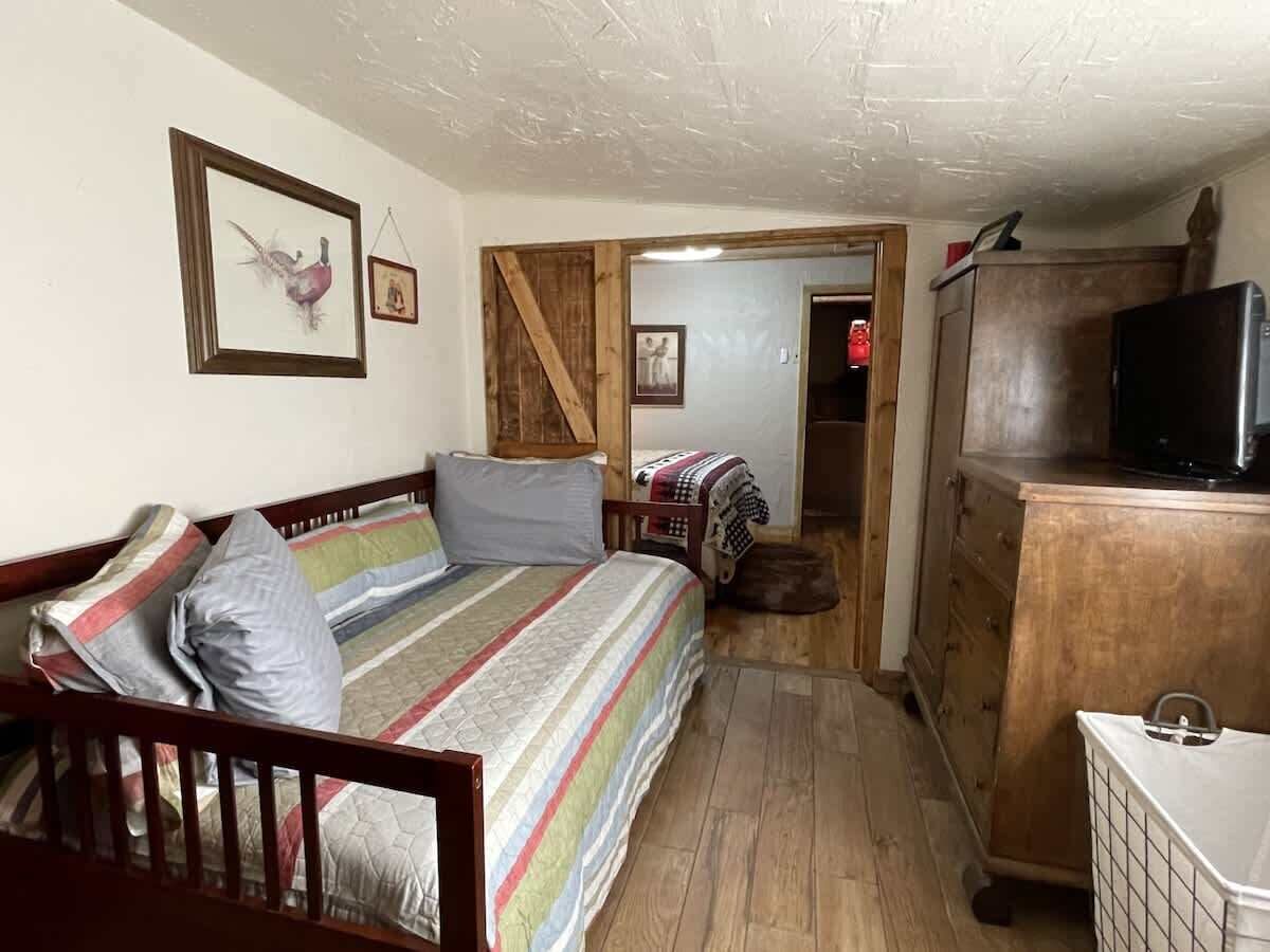 A small, cozy room with a bed, a wooden dresser, a television, and a door leading to another room.