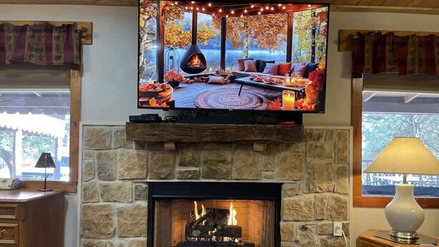 A stone fireplace with a TV above it, a wooden bench, and a lamp on a side table. - Midtown Meadow Cabin (Ruidoso)