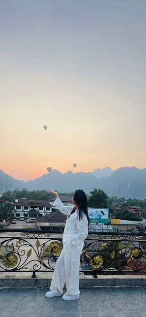 A person standing on a balcony overlooking a town with mountains in the background. - Khampaseuth Hotel (Vang Vieng)