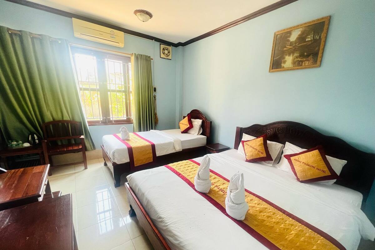 A hotel room with two beds, a desk, a chair, and a window with curtains.