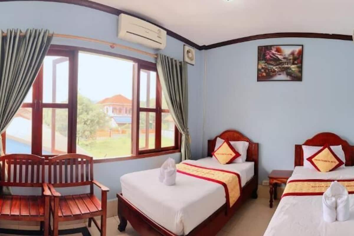 A room with two beds, a wooden desk, and a window with curtains.