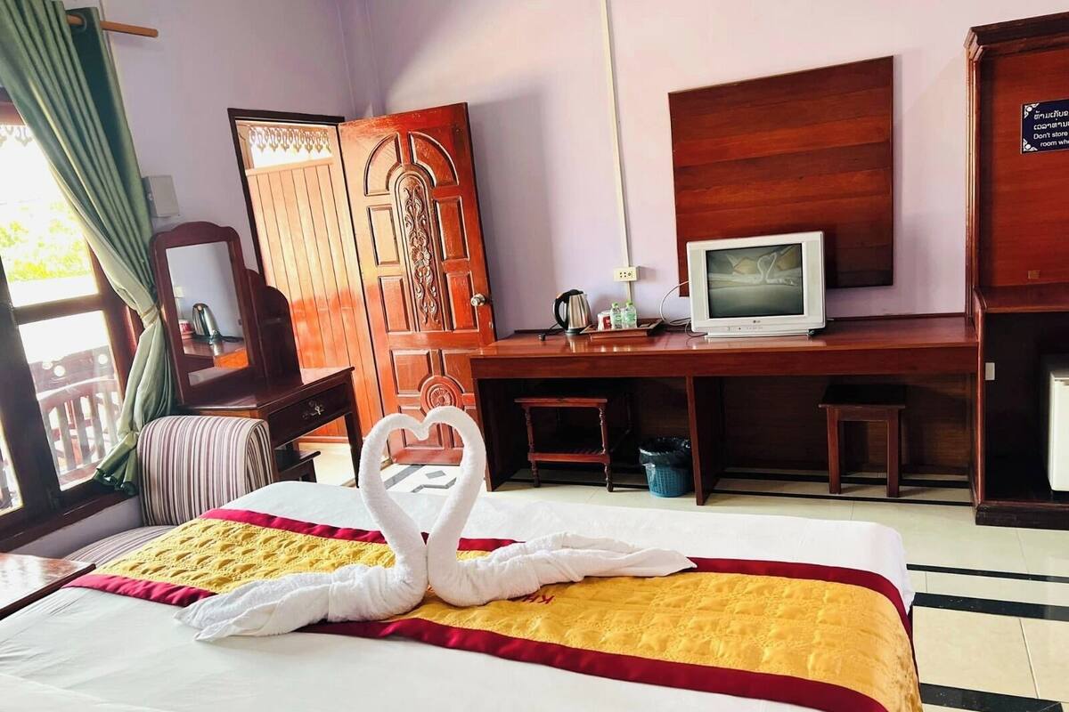 A hotel room with a bed, a desk, a television, and a wooden wardrobe.