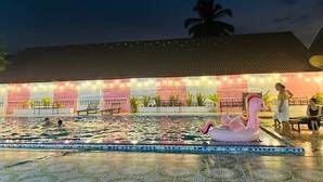A swimming pool with a pink flamingo float, a brick wall, and string lights. - Khampaseuth Hotel (Vang Vieng)