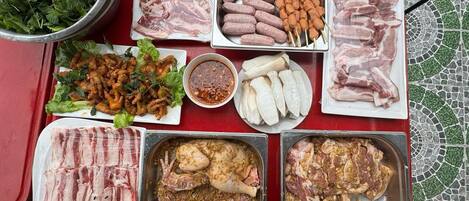 A table with various food items including raw meats, sausages, and vegetables, suggesting a barbecue setting.