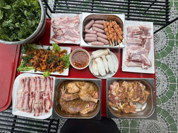 A table with various food items including raw meats, sausages, and vegetables, suggesting a barbecue setting. - Khampaseuth Hotel (Vang Vieng)