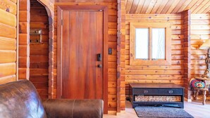 A wooden cabin interior with a large wooden door, a leather sofa, a small table, and a window.