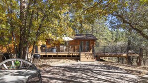 A rustic cabin with a wooden deck, surrounded by trees.