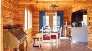 A wooden cabin interior with a dining table, chairs, a kitchen area, and a small bar.