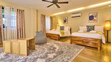 A hotel room with two beds, a ceiling fan, a large rug, and a wooden side table.