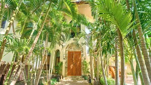 A pathway flanked by tall palm trees leading to a building with a large wooden door. - Dos Maya by Araw Residences (Nasugbu)