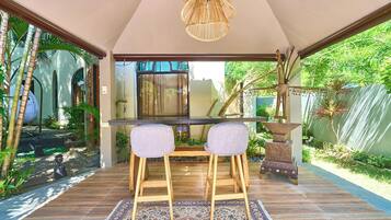 A dining area with a table and two chairs, a hanging light fixture, and a view of a garden with plants and a fence.